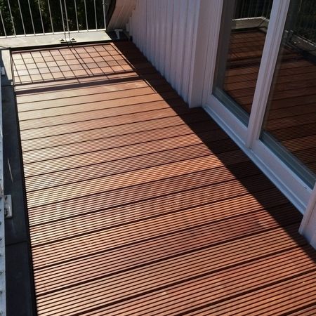 Holzdeck mit Balkon und Fenster, umgeben von einer ruhigen Umgebung.